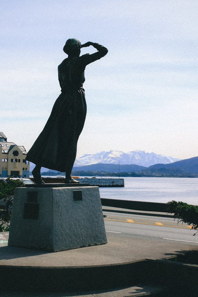 A statue gazes over the fjord in Alesund, Norway, with snowy mountains in the background.